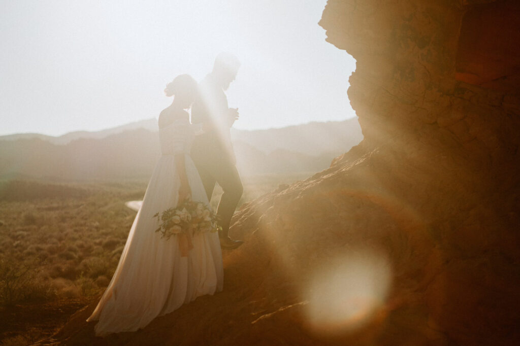 Bride and Groom walking together on the rocks at Valley of Fire. The sun is setting and glowing behind them.